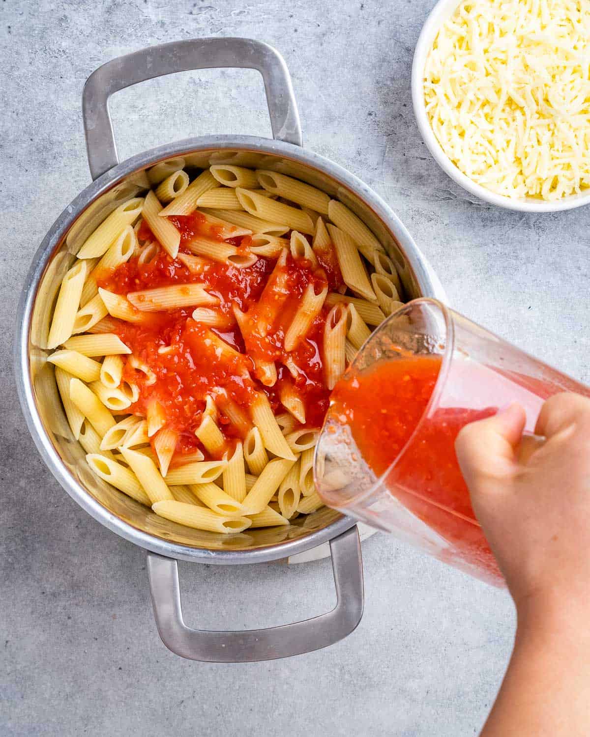 Pouring marinara sauce over cooked pasta.