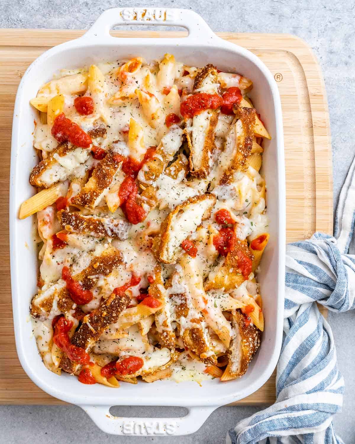 A baking white dish with pasta and tomato sauce topped with crispy chopped chicken and melted cheese.