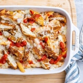 a baking white dish with pasta and tomato sauce topped with crispy chopped chicken and melted cheese.