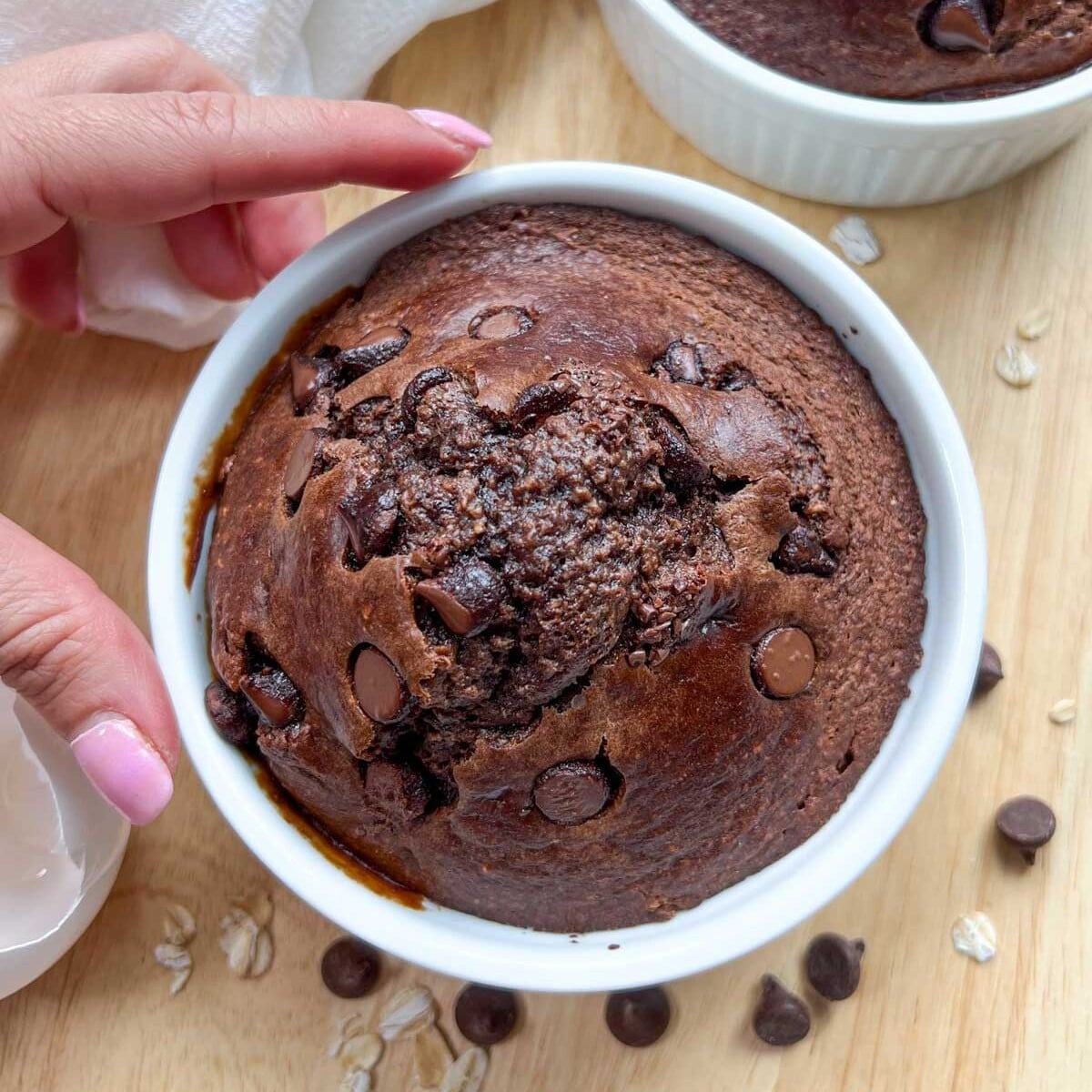 one hand holding a ramekin with chocolate baked oats.