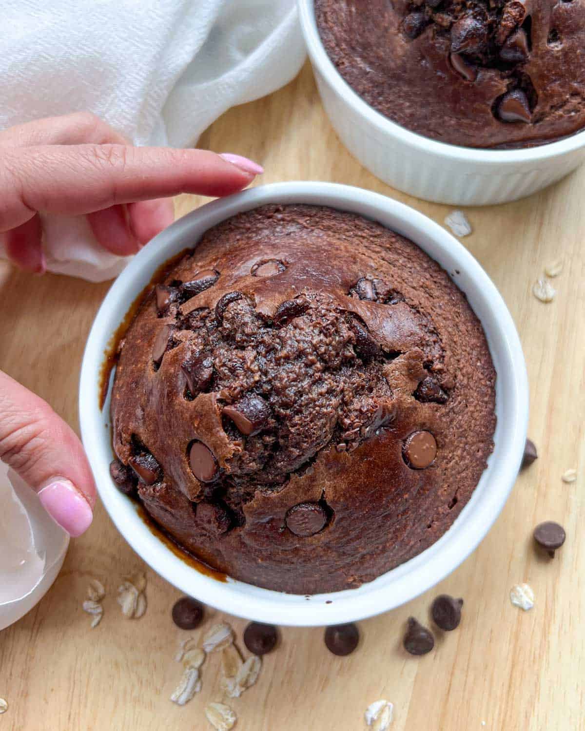 one hand holding a ramekin with chocolate baked oats.