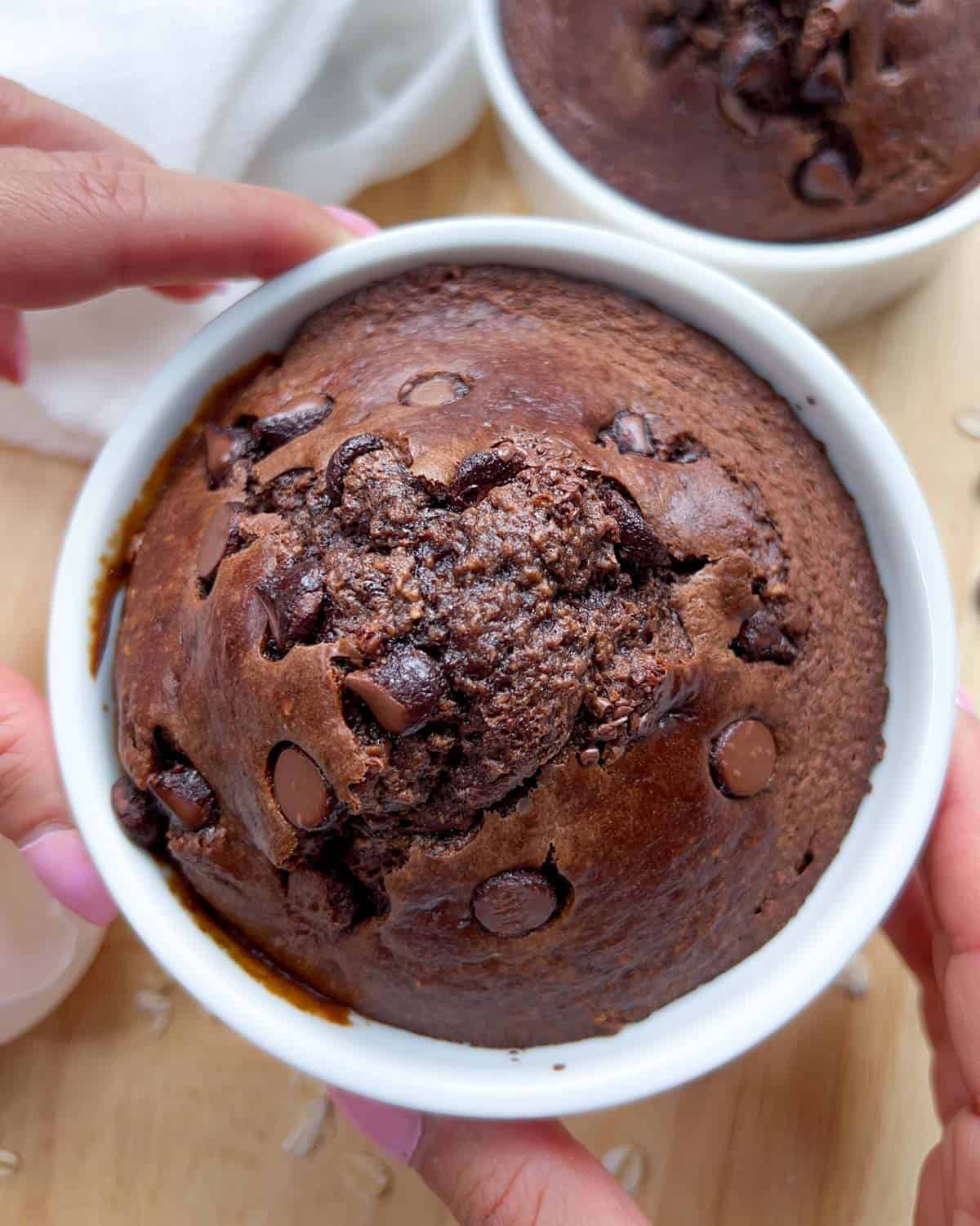 hand holding a ramekin with chocolate baked oats that look like a brownie cake.