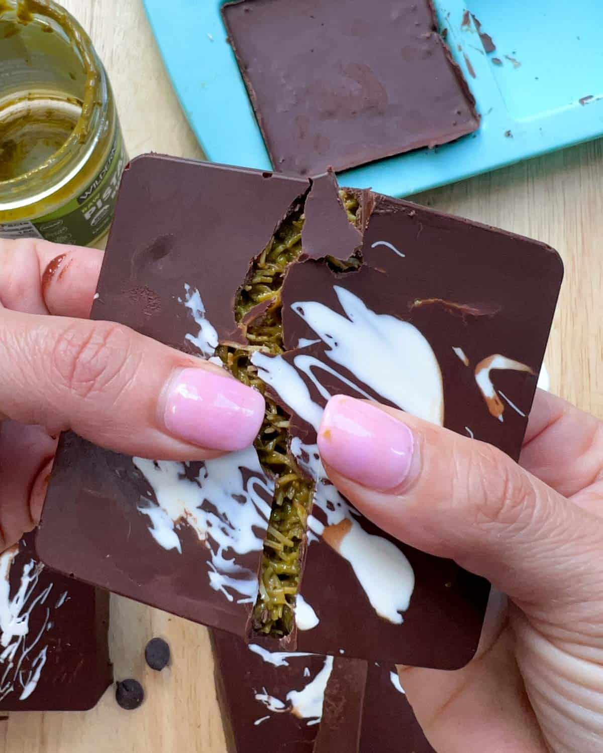 hand breaking a chocolate bar in half and showing the green pistachio filling.