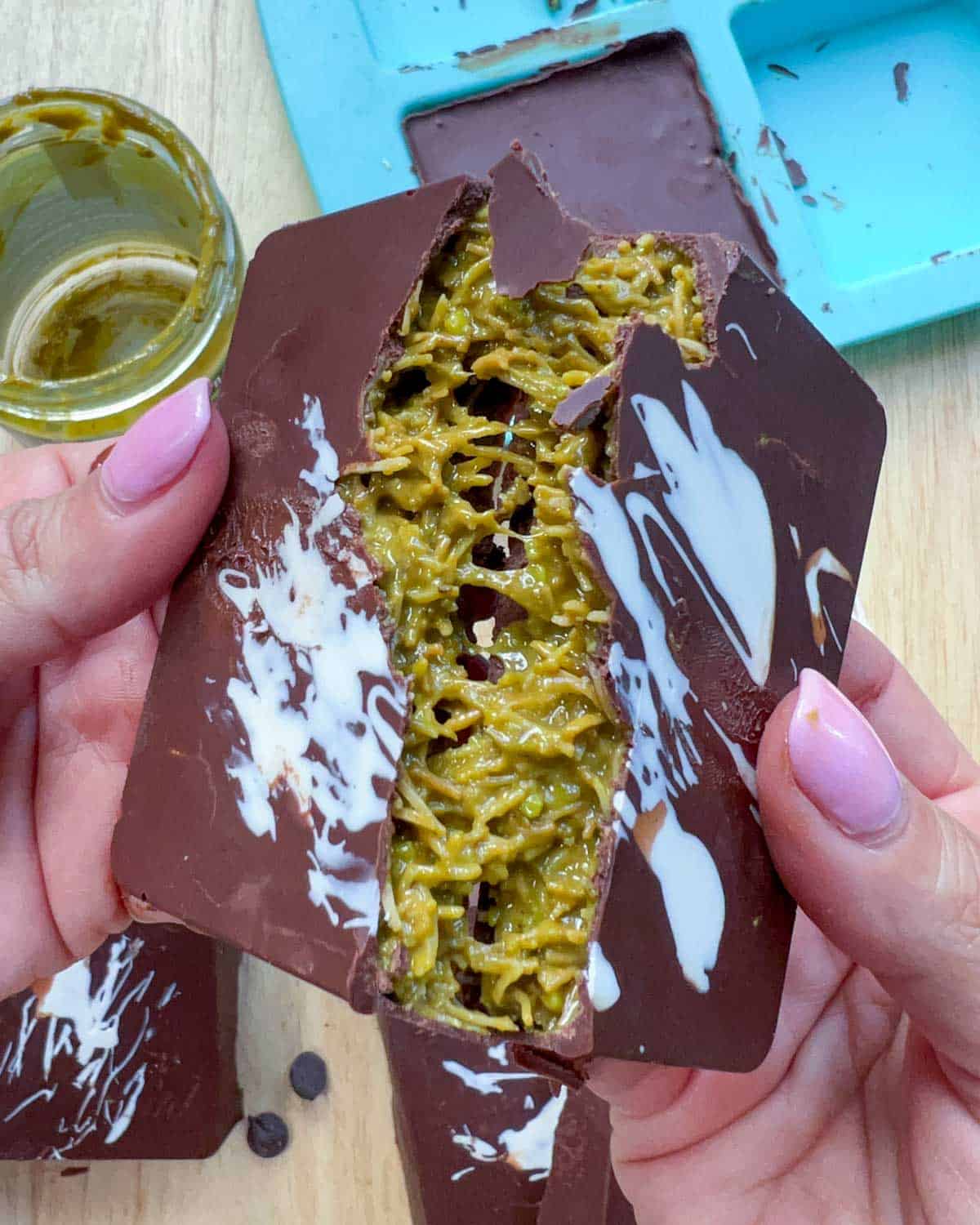 hand breaking a bar of chocolate and showing the green pistachio filling.