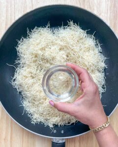 Adding coconut oil to the kataifi in the pan.