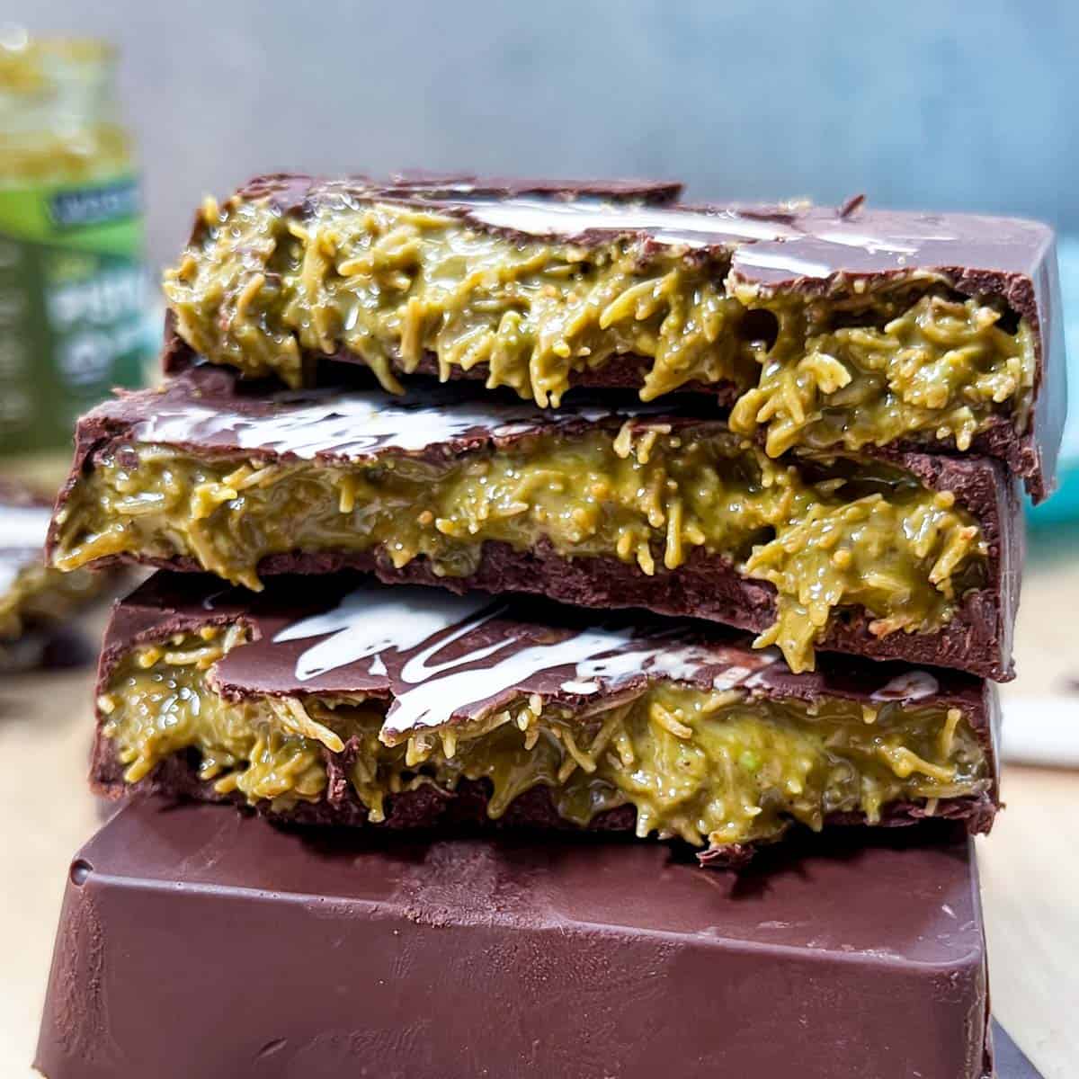 3 halved chocolate bars stuffed with pistachio cream are stacked over each other on a cutting board.