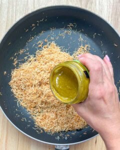 pouring pistachio butter over kataifi in pan.