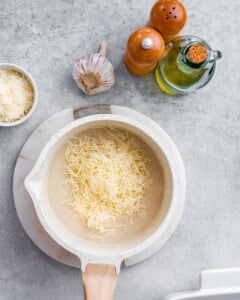 Shredded cheese is added to a pot with white sauce for mac and cheese.