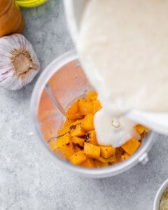 Pouring milk into a blender with roasted butternut squash.