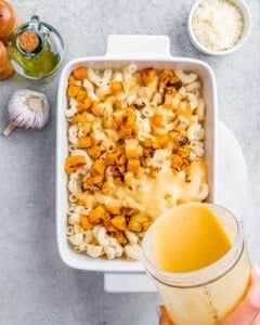 Pouring sauce over macaroni noodles in a white baking dish.