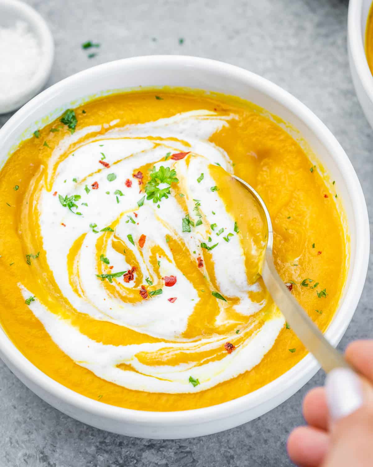 A white bowl of carrot ginger soup swirled with yogurt.