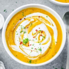 carrot soup in a round bowl topped with sour cream swirls and chili flakes.