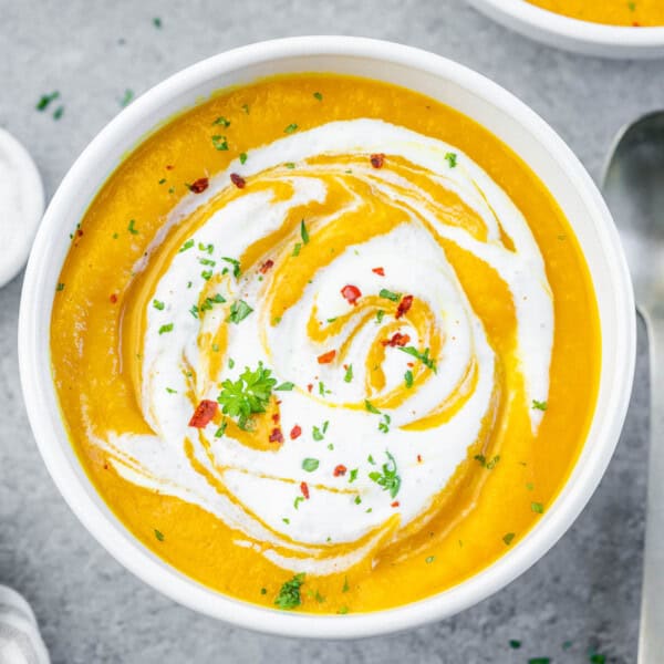 carrot soup in a round bowl topped with sour cream swirls and chili flakes.