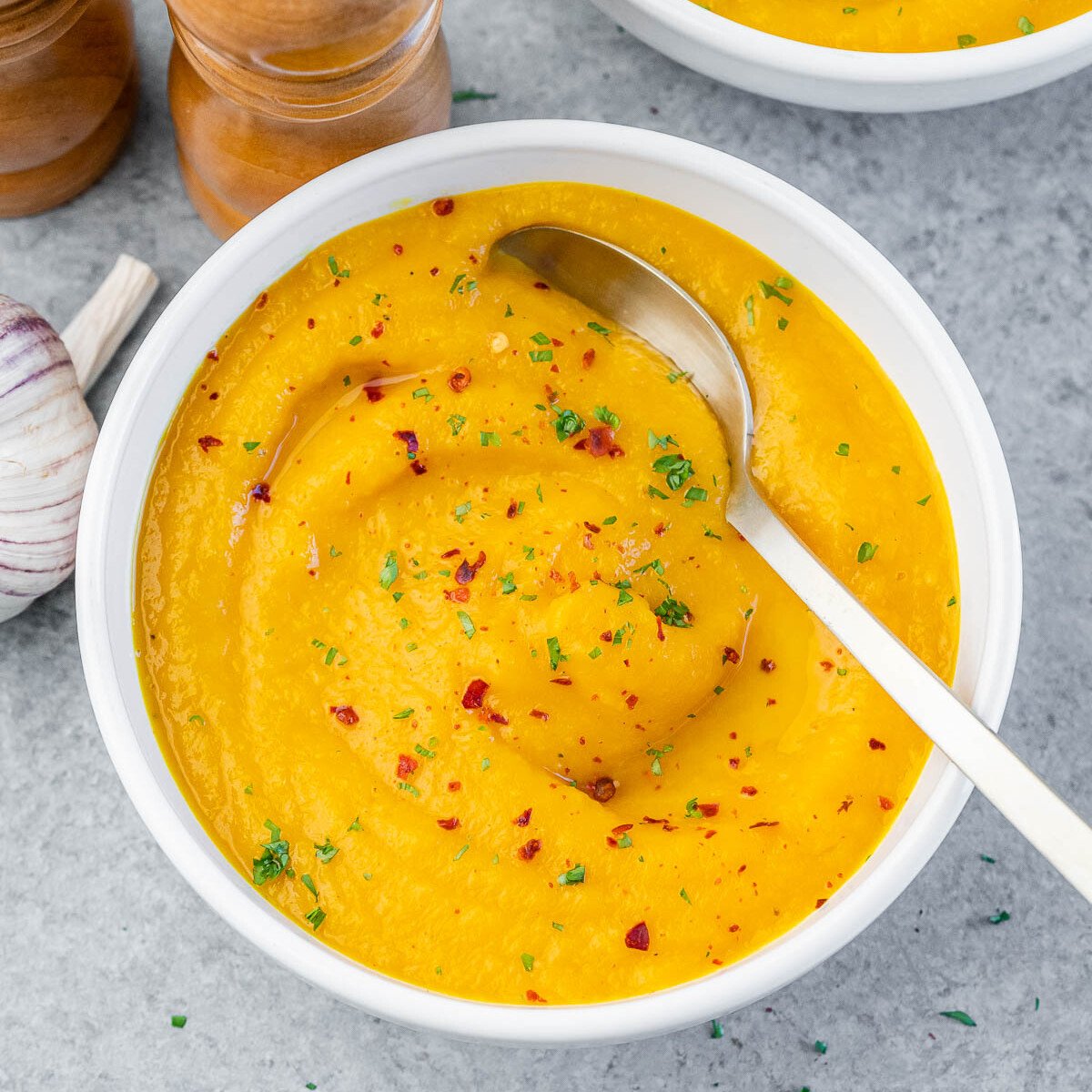 A white bowl of carrot ginger soup with chili flakes and a spoon.
