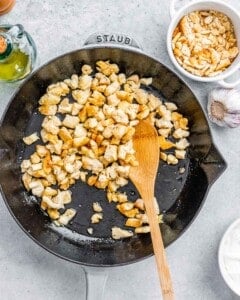 Chicken pieces sautéing in a black skillet with a wooden spoon before adding the vegetables.