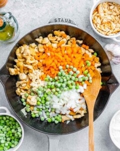 Onions, carrots, and peas added to a skillet with chicken, ready to be sautéed together for the filling.