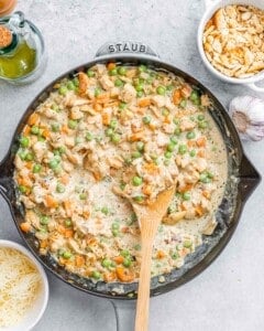 Overhead view of the creamy sauce simmering in a cast iron skillet with chicken, peas, carrots, and onions.