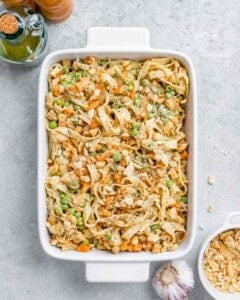 Overhead shot of the casserole baked to a golden brown, sitting on a light gray surface with a full head of garlic and a small bowl of crackers beside it.