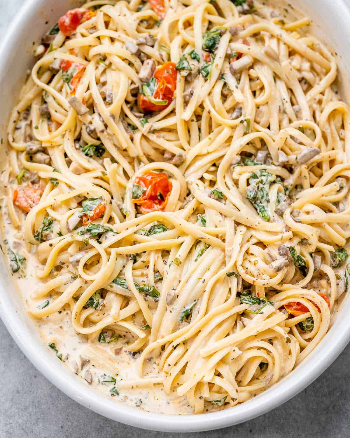 creamy spaghetti with tomato and spinach in an oval dish.