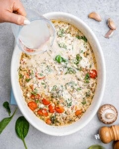 pasta water being added to the creamy tomato sauce in a white dish.