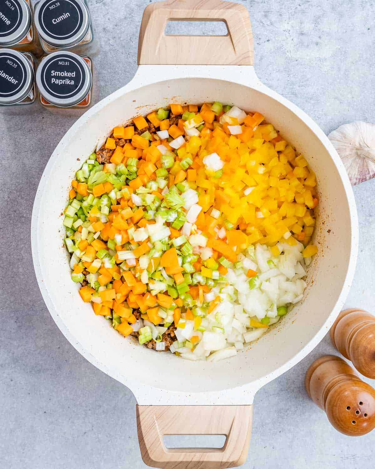 Adding veggies to browned beef in a pot.