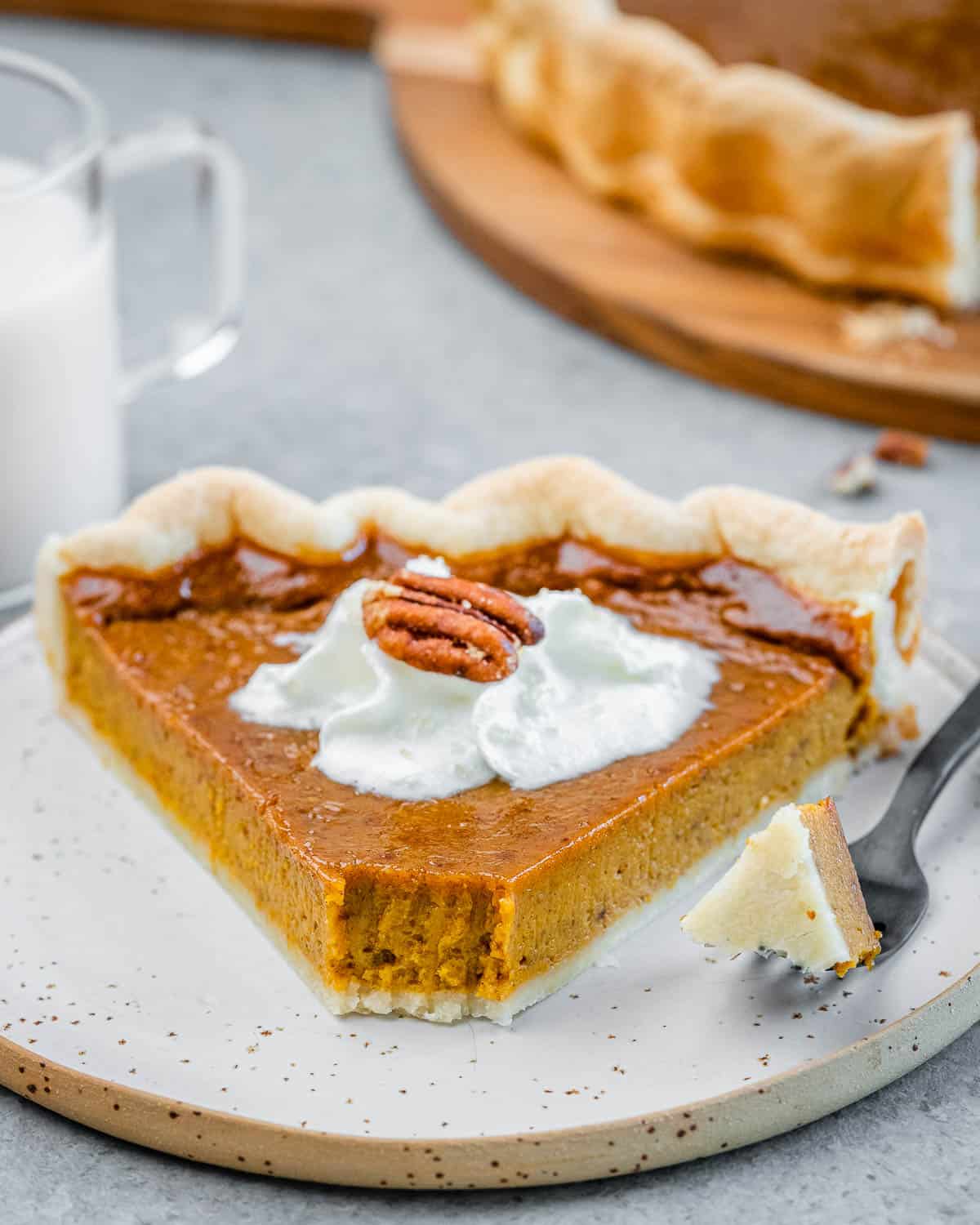 A slice of pumpkin pie on a plate with a bite taken off it.