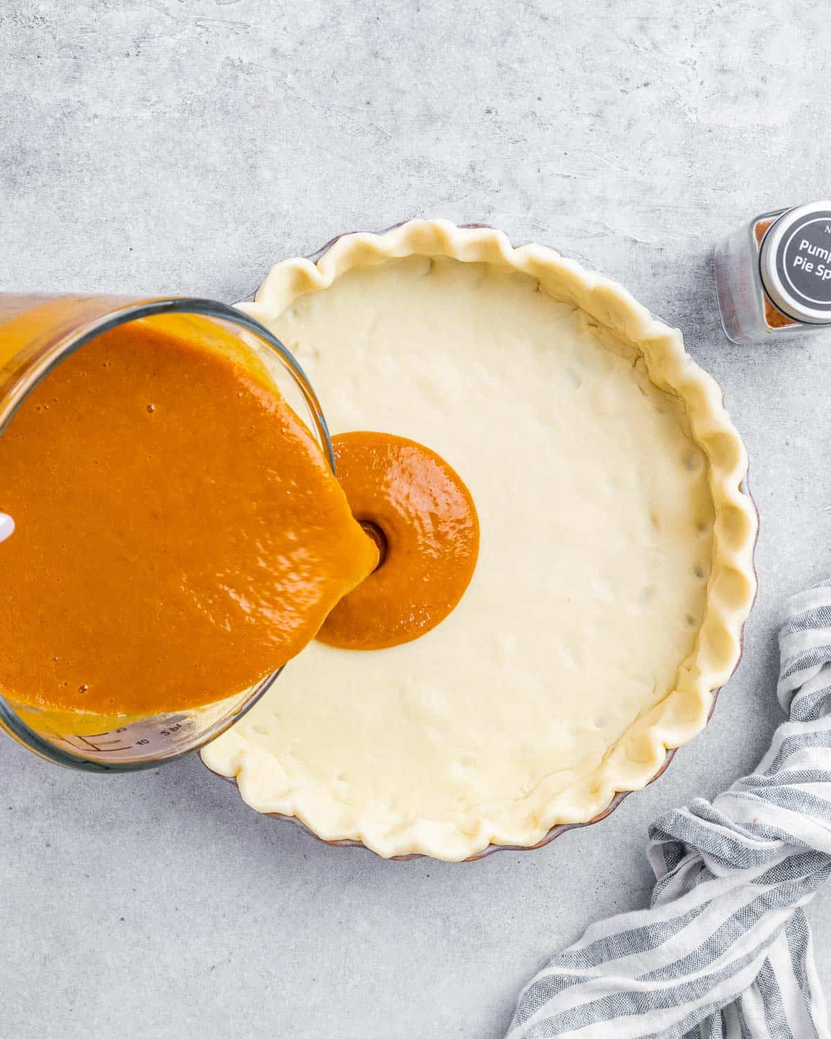 Pouring pumpkin pie filling into a pie crust.