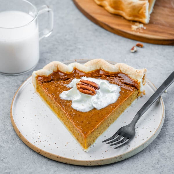 A slice of pumpkin pie on a white plate with a fork by it.