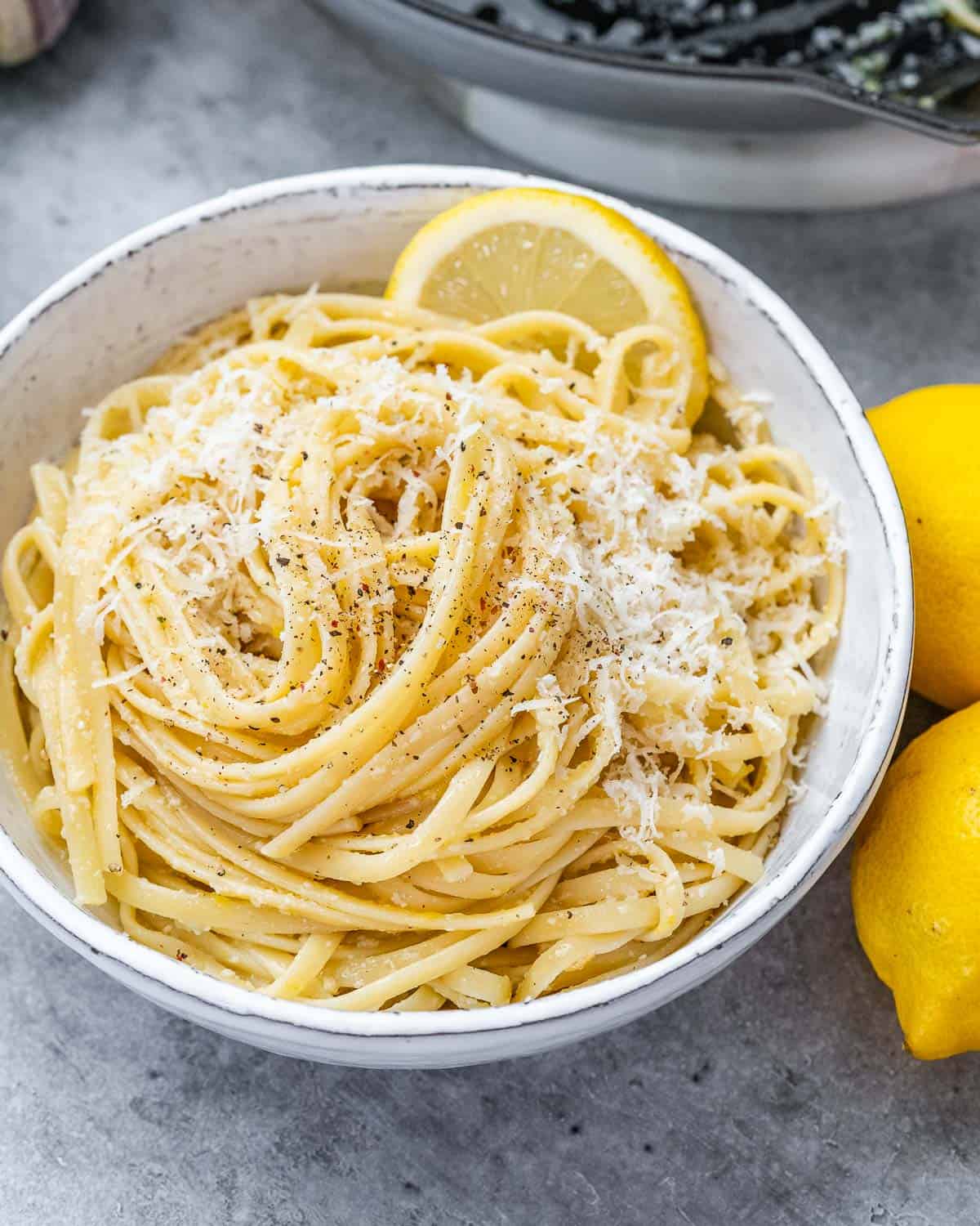 Close up of Pasta la Limone in a white bowl, surrounded by fresh lemons.