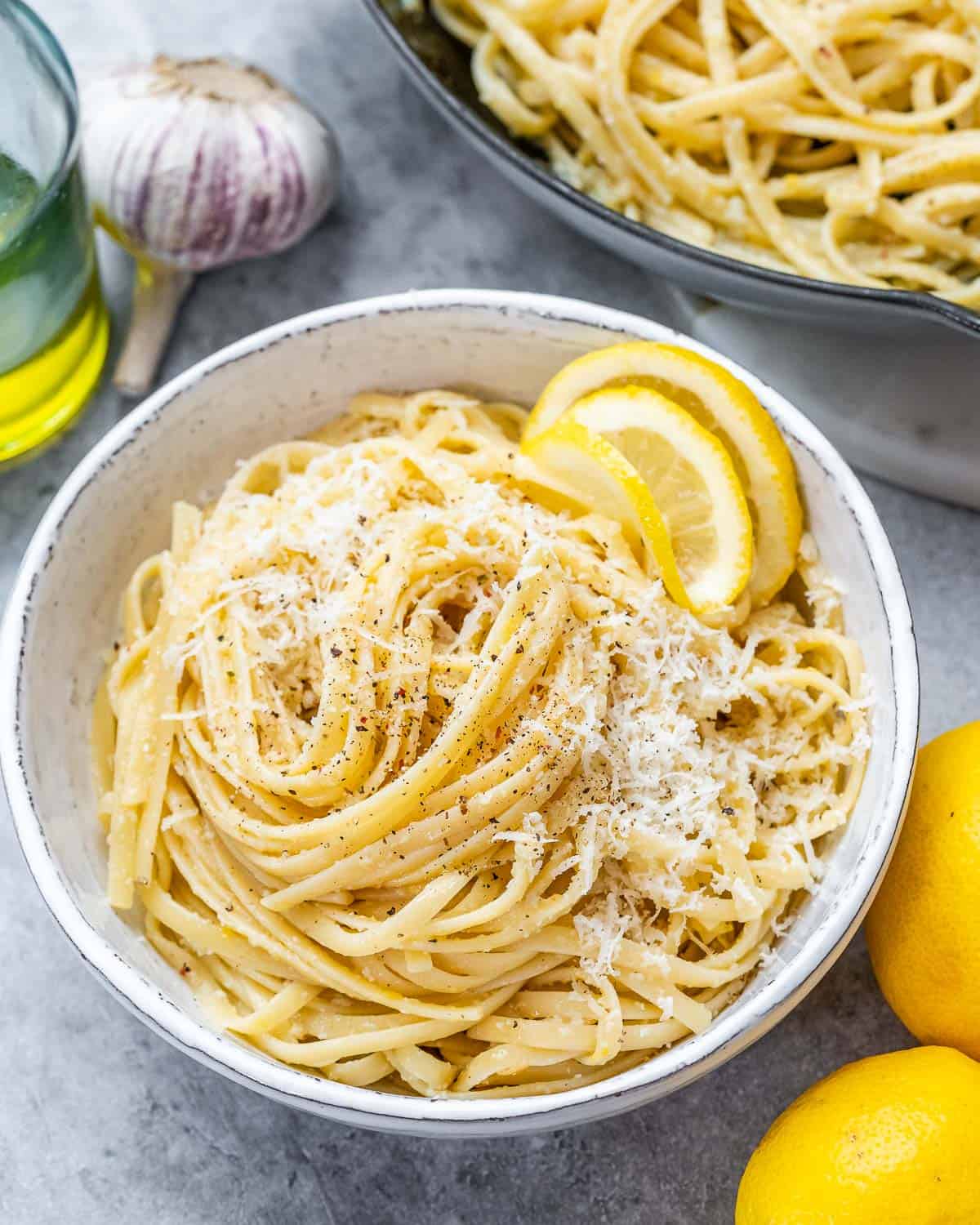 Cooked pasta limone in a white bowl topped with grated parmesan and lemon slices.