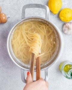 Cooked linguine being lifted from boiling salted water with kitchen tongs.