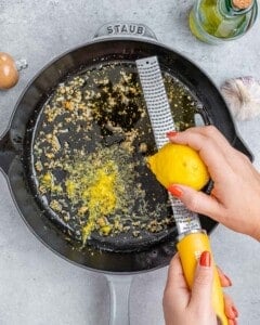 Garlic sautéing in olive oil with lemon zest being added into the pan.