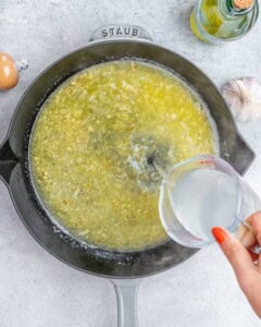 Starchy pasta water being poured into the skillet to loosen the lemon sauce.