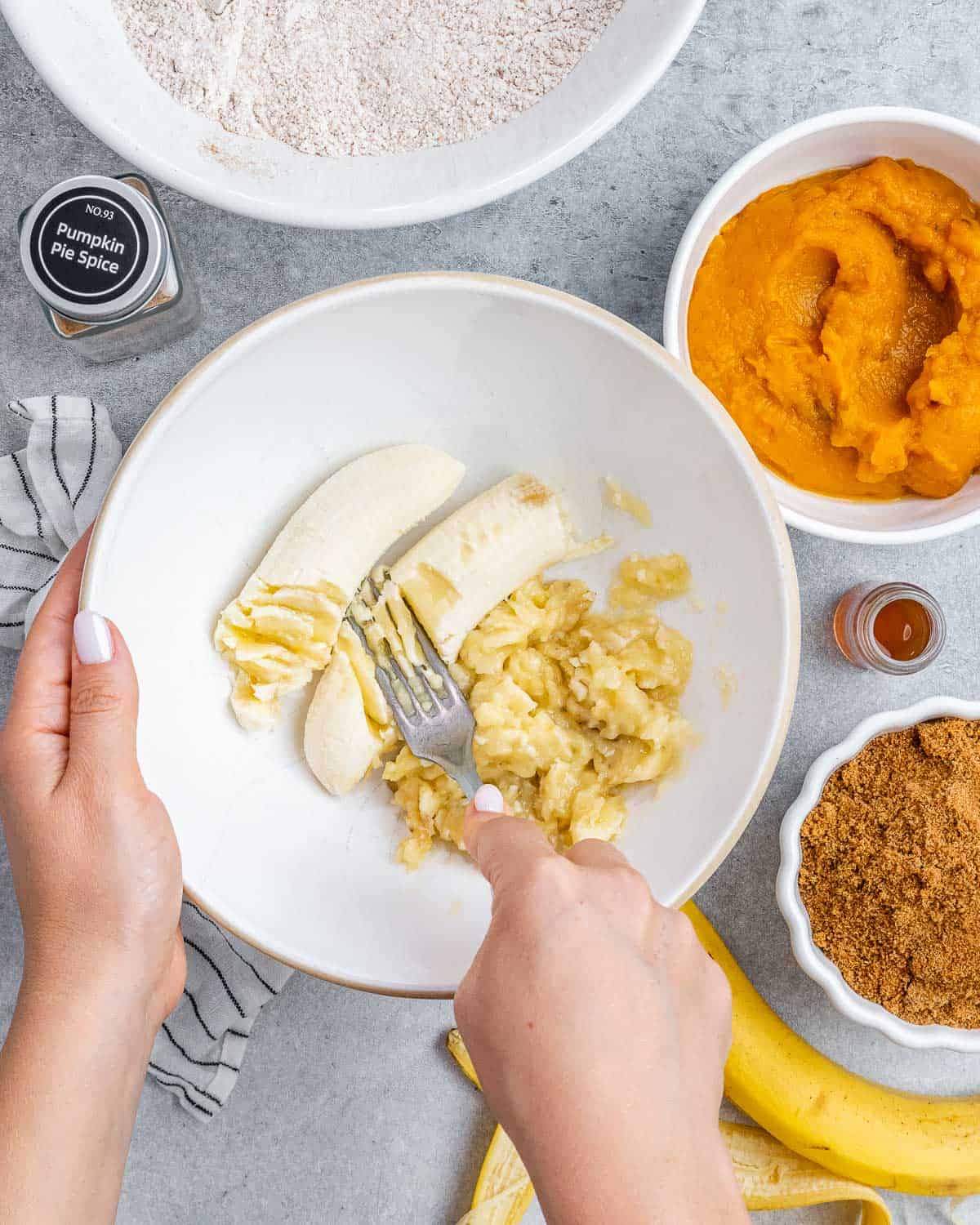 Mashing bananas with a fork in a white bowl.