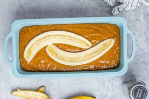 Pumpkin bread batter in a loaf pan, topped with banana slices.