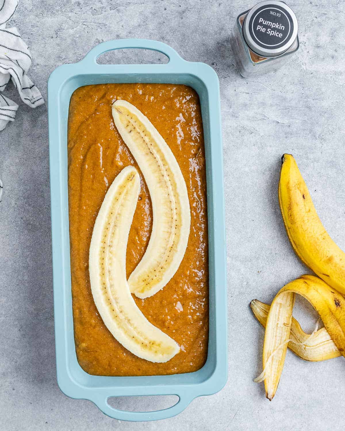 Pumpkin bread batter in a loaf pan, topped with banana slices.