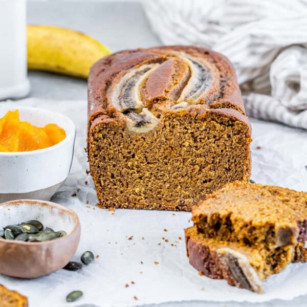 Pumpkin bread on a flat surface with two slices sliced off.