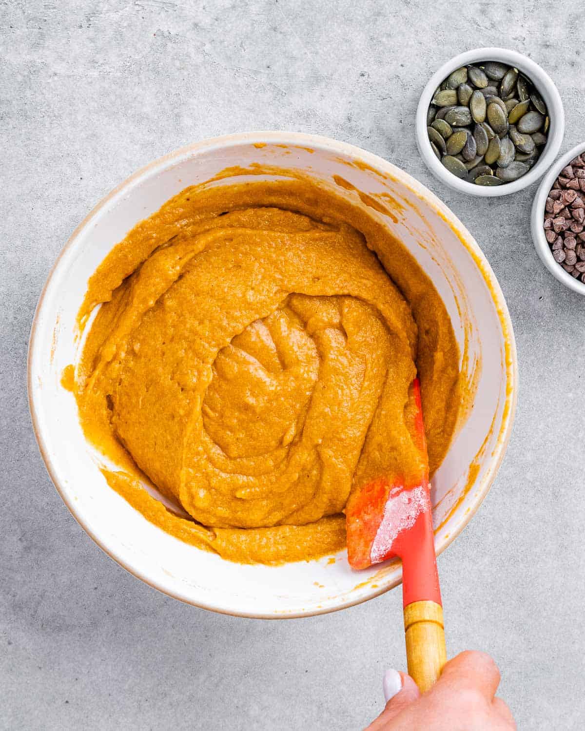 Stirring pumpkin cake batter in a white mixing bowl.