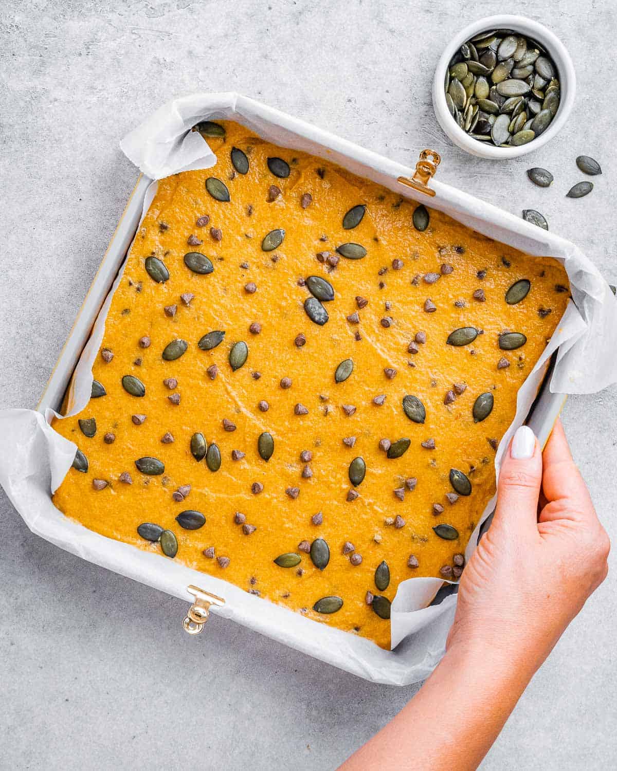 Pumpkin seeds sprinkled over an unbaked pumpkin cake in a square pan.