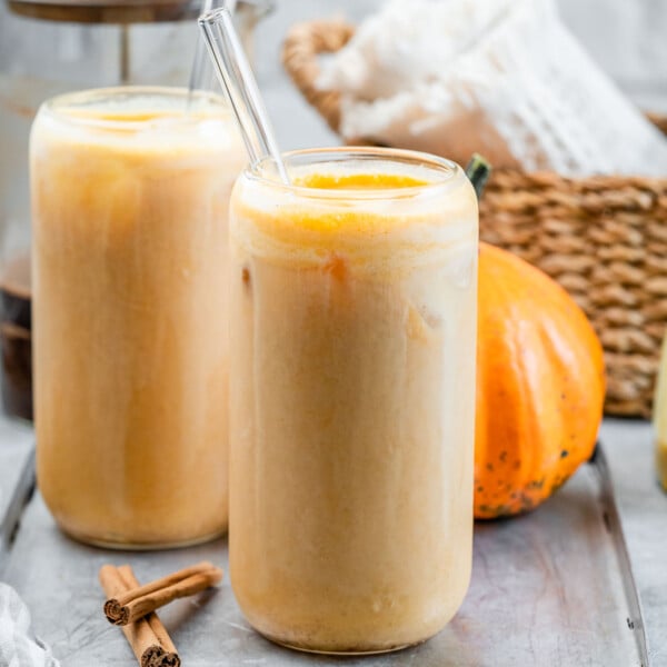 Two glasses of pumpkin latte with glass straws in them.