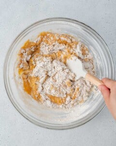 dry ingredients added over wet ingredients and being mixed in a bowl.