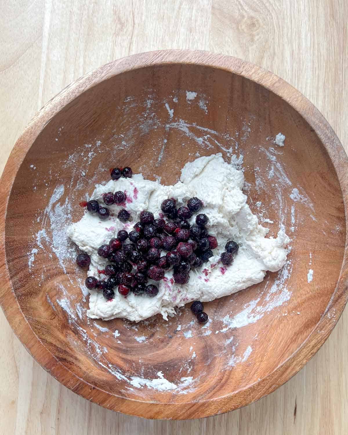 blueberries added to the bagel dough in a brown bowl.