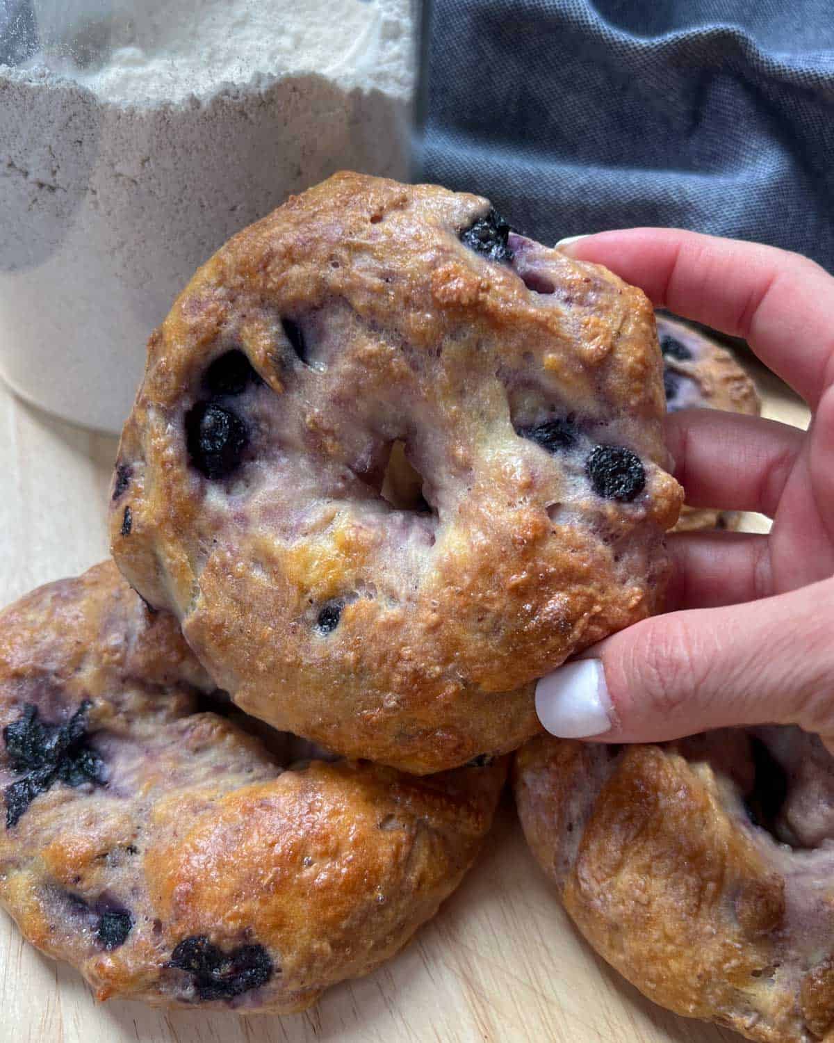 hand holding a blueberry bagel over another bagel.