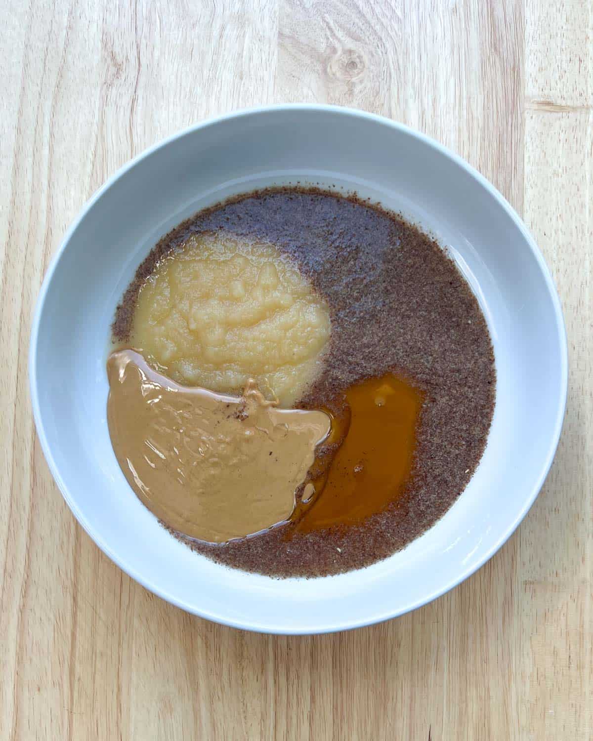 a bowl with flaxseed, peanut butter, apple sauce, and maple syrup. Before mixing.