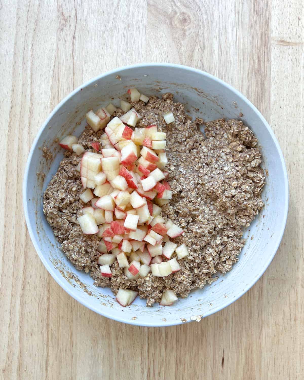 chopped apples are added over the oat mixture in a round bowl.