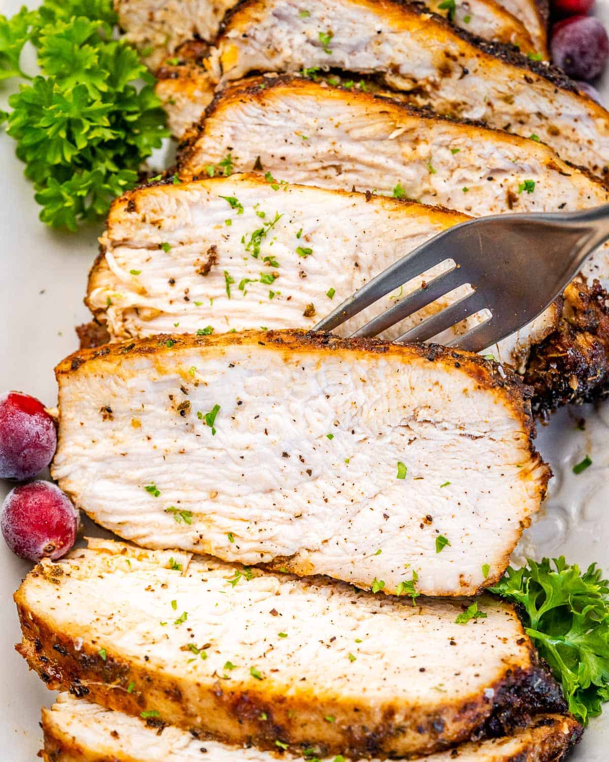 fork grabbing a slice of cooked turkey breast on a plate.