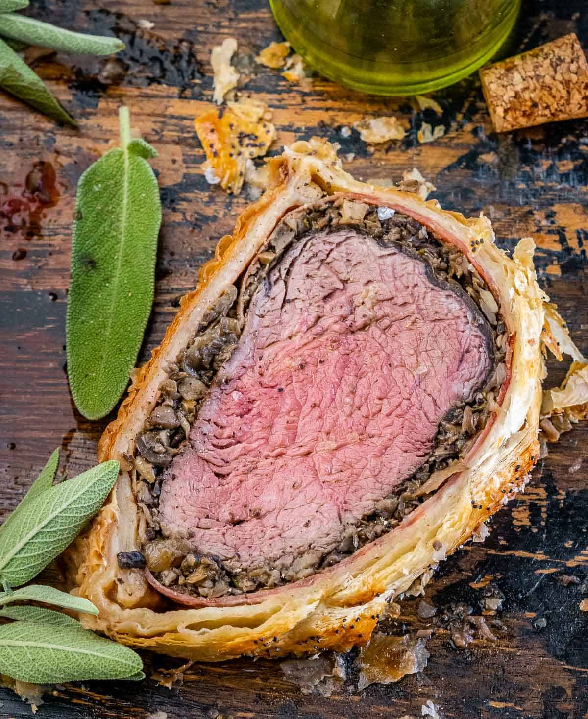 A slice of beef wellington on a brown cutting board.