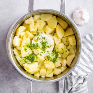 A sprinkle of parsley, Boursin cheese and olive oil added to potatoes in a pot.