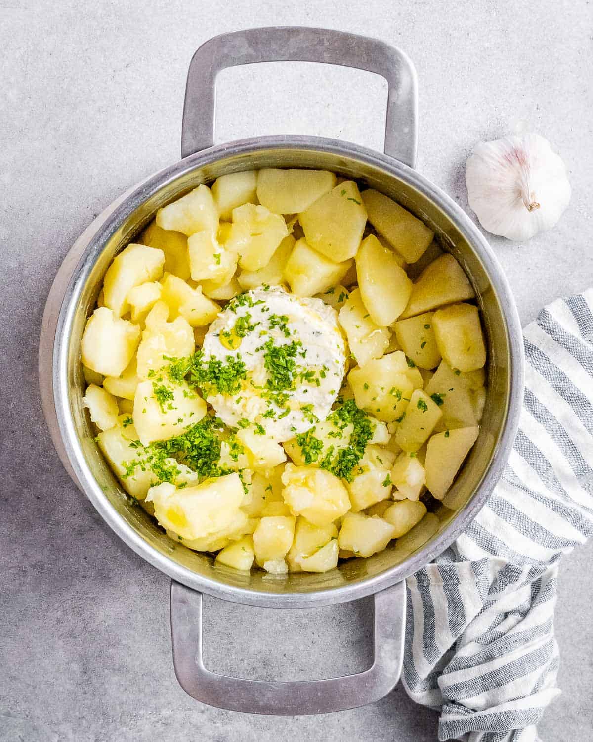 A sprinkle of parsley, Boursin cheese and olive oil added to potatoes in a pot.