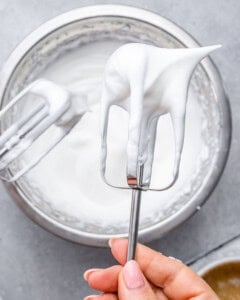 Electric mixer beaters holding glossy, stiff egg whites ready for folding.